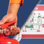 Main tenant un extincteur au premier plan avec un plan d’intervention incendie d’ERP affiché en arrière-plan, montrant les accès, issues de secours et équipements de sécurité.